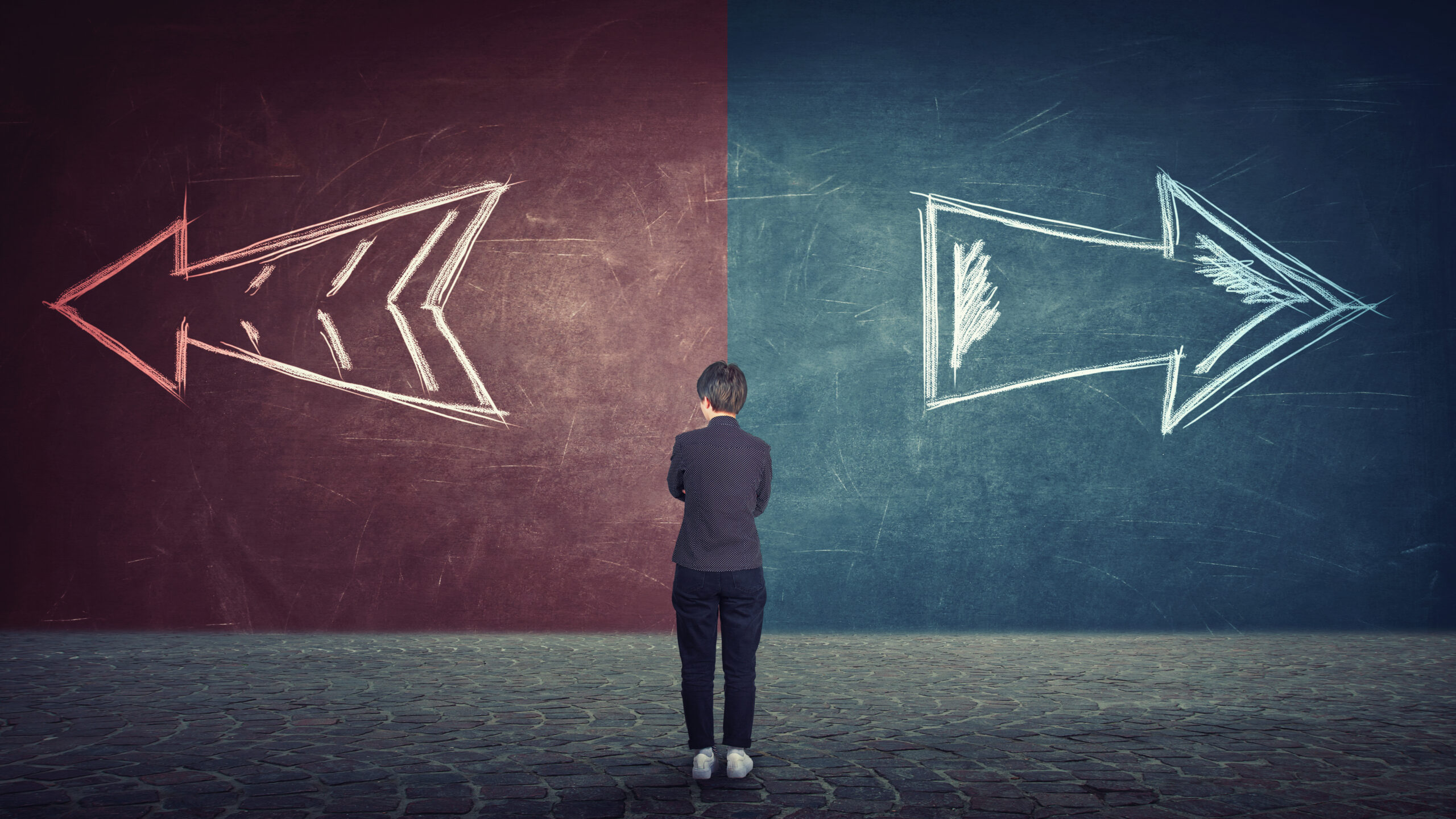 Rear view of doubtful businesswoman in front of a split wall as arrows leads in two different ways red and blue side. Correct choice left or right, failure or success. Difficult decision concept.