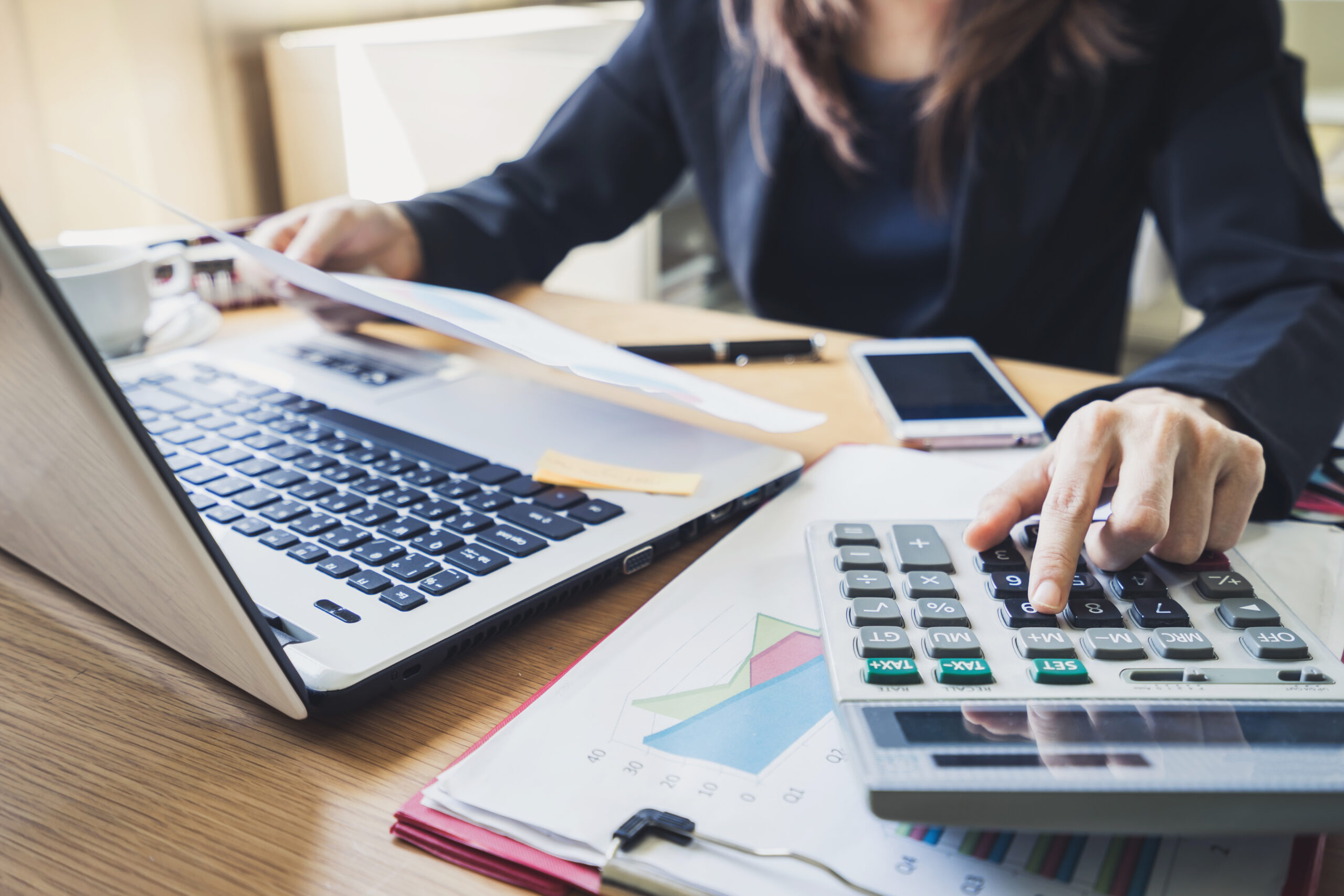 woman working out business costs on large calculator with laptop