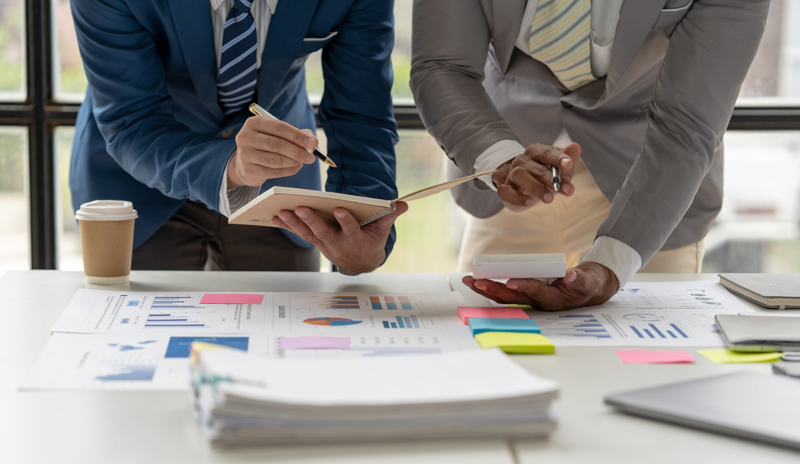 two businesspeople comparing notes and making calculations over a desk with scattered graph paper